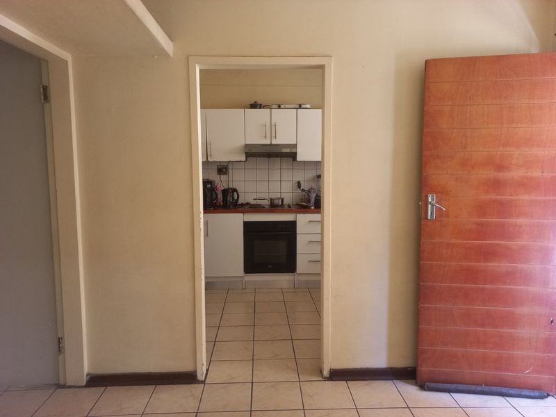 A view through a doorway into a functional kitchen featuring white cabinetry, tiled backsplash, built-in oven, and hob with tiled flooring throughout.