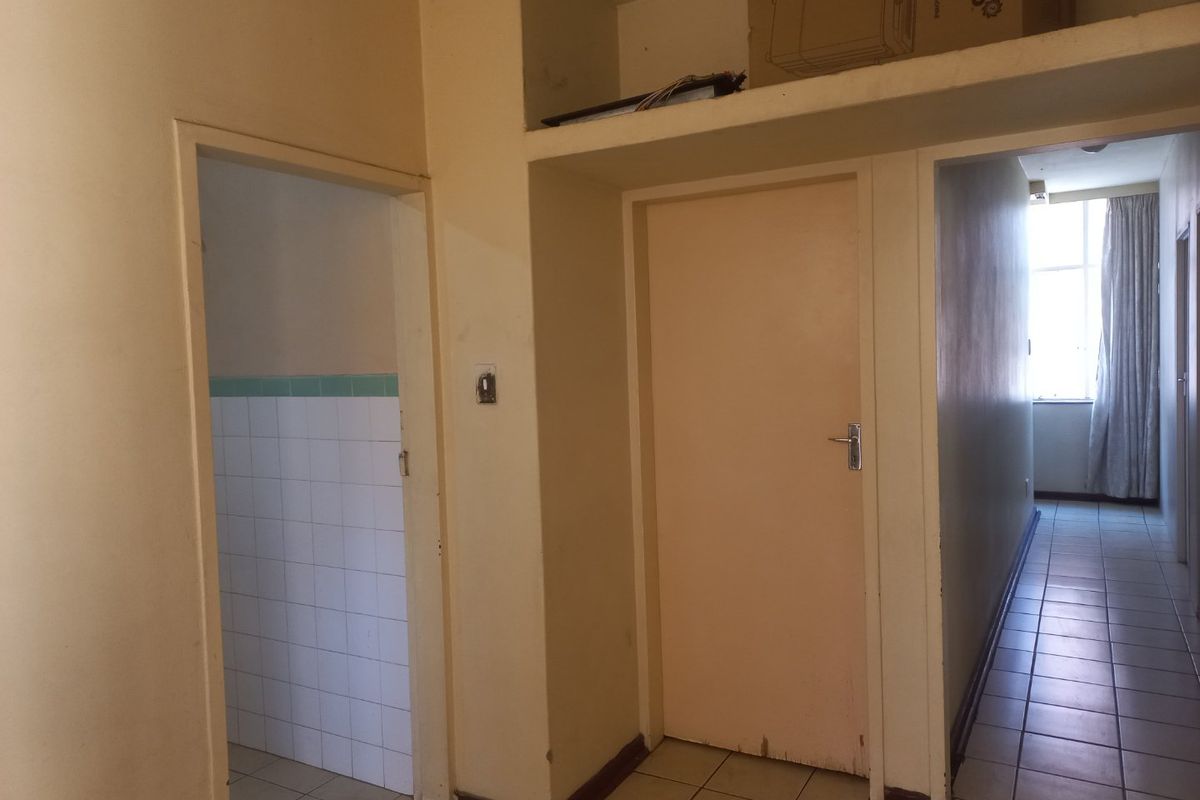 A functional hallway area featuring tiled flooring, internal doors, and overhead built-in storage space, providing access to adjacent rooms within the apartment.