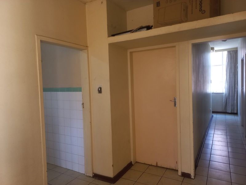 A functional hallway area featuring tiled flooring, internal doors, and overhead built-in storage space, providing access to adjacent rooms within the apartment.