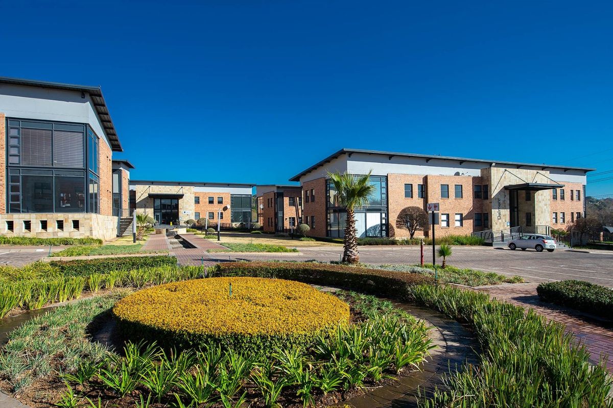 A professional exterior view of a modern commercial office park featuring brick facades, paved parking areas, and well-maintained landscaped gardens.