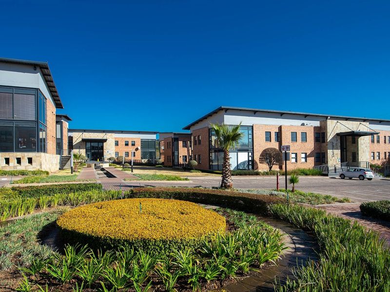 A professional exterior view of a modern commercial office park featuring brick facades, paved parking areas, and well-maintained landscaped gardens.
