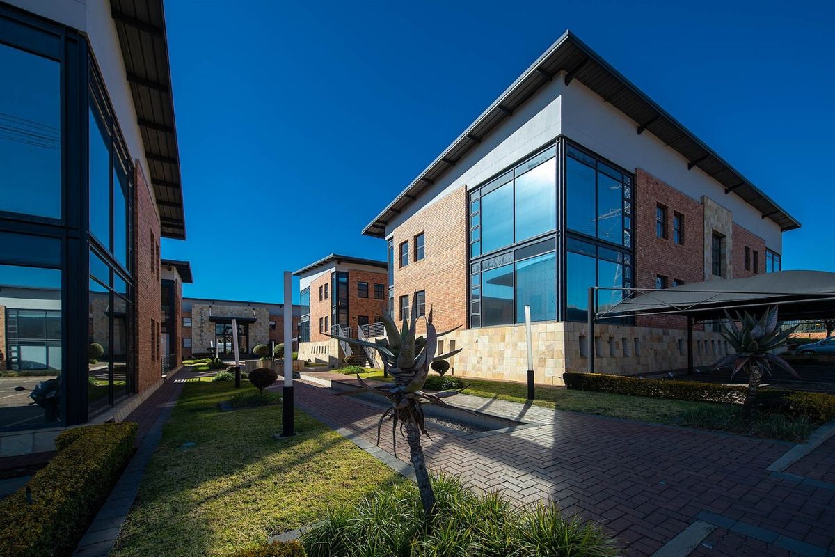 Modern commercial office complex featuring brick and glass facades, paved walkways, and well-maintained landscaped grounds.