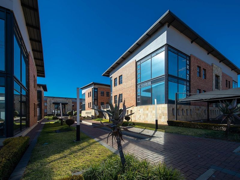 Modern commercial office complex featuring brick and glass facades, paved walkways, and well-maintained landscaped grounds.