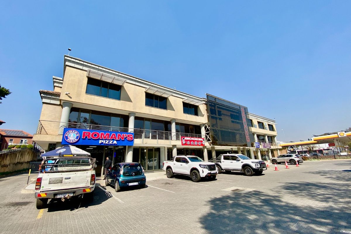 Front exterior view of a multi-level commercial building featuring paved parking, glass facade elements, and prominent commercial signage.