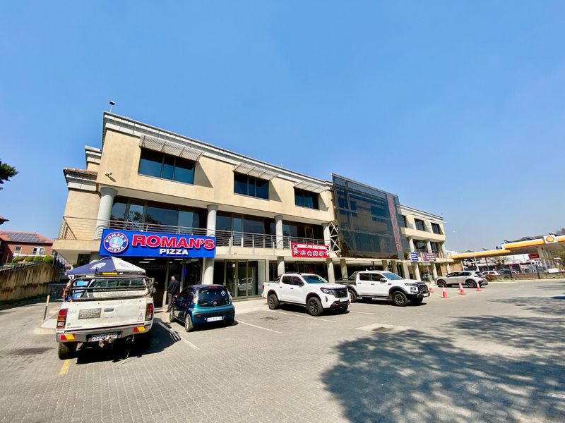 Front exterior view of a multi-level commercial building featuring paved parking, glass facade elements, and prominent commercial signage.