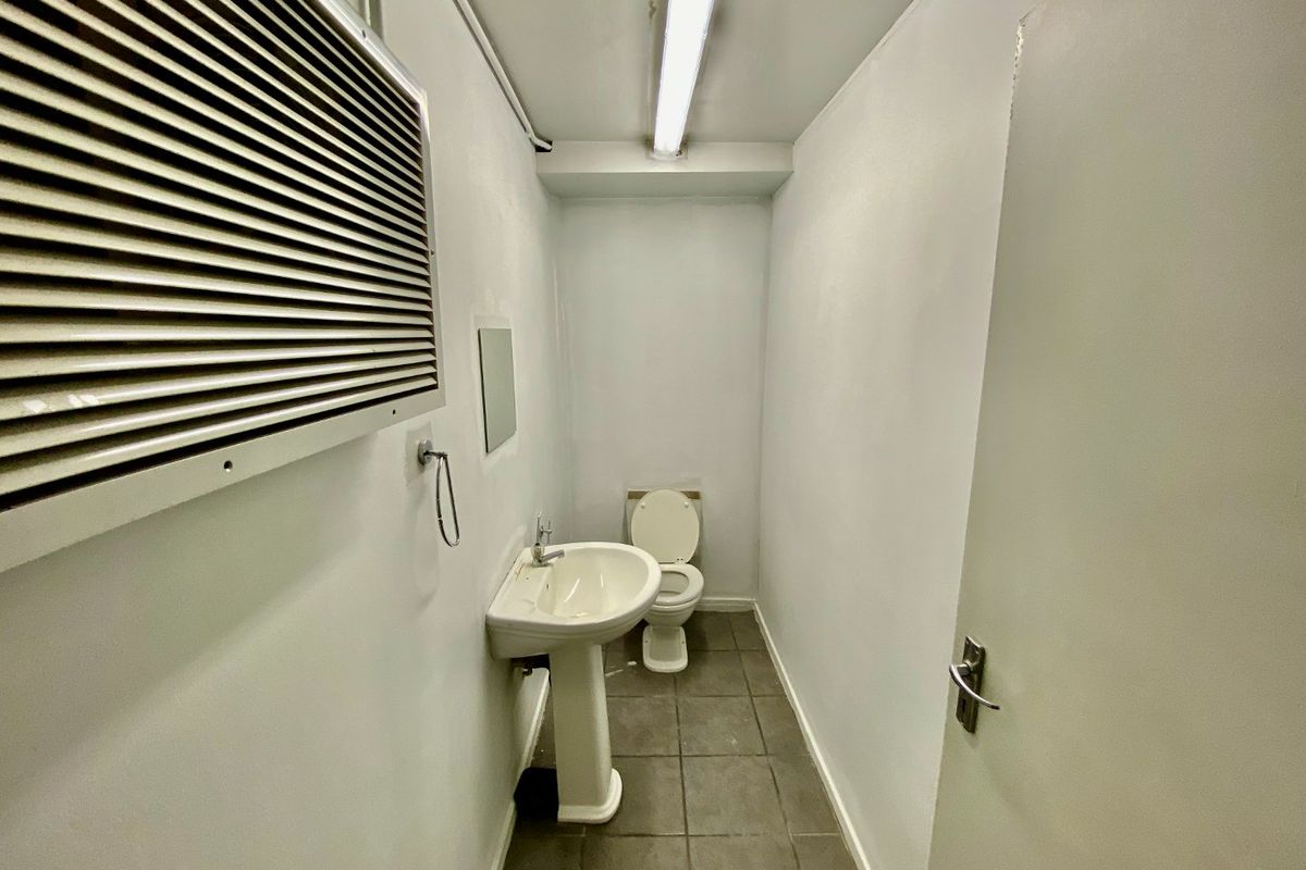 A functional commercial restroom featuring a pedestal sink, toilet, tiled flooring, and basic utility lighting.