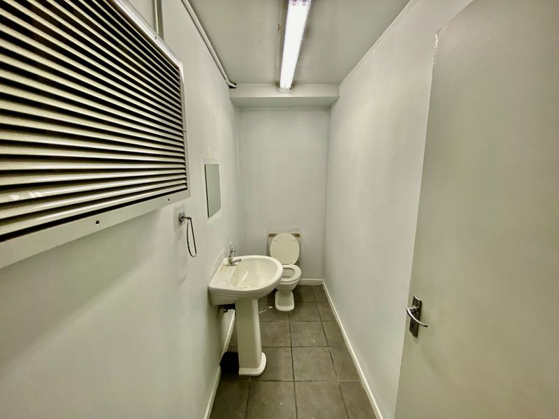 A functional commercial restroom featuring a pedestal sink, toilet, tiled flooring, and basic utility lighting.