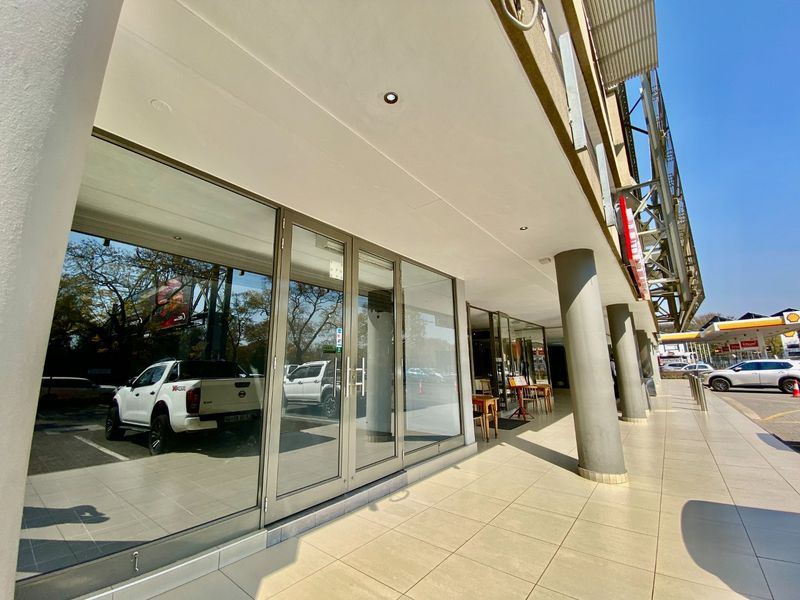 Commercial storefront featuring large glass panels, aluminum framing, and a covered tiled walkway with structural support columns.