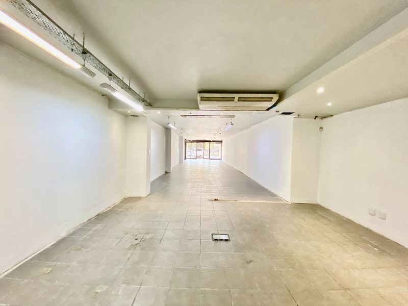 Spacious open-plan commercial retail or office space featuring tiled flooring, exposed industrial-style lighting, and a ceiling-mounted air conditioning unit.