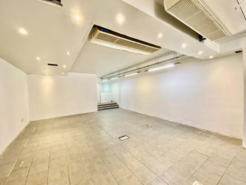A vacant open-plan commercial space featuring tiled flooring, recessed downlights, track lighting, and integrated ducted air conditioning units.