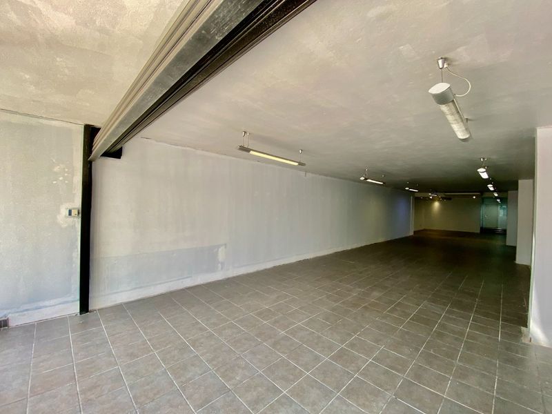 A spacious, empty commercial utility area featuring tiled flooring, exposed structural beams, and functional strip lighting, ready for custom fit-out.