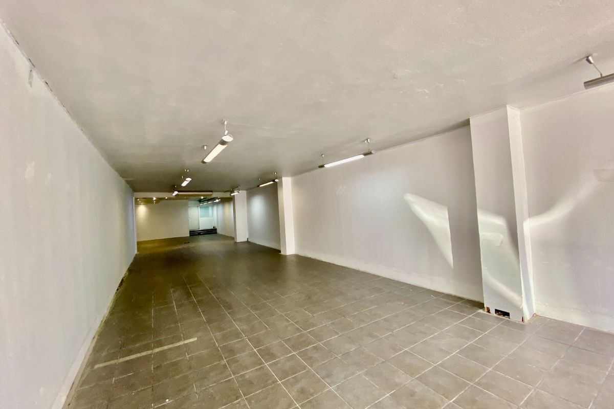 A vacant, open-plan commercial space featuring tiled flooring, structural columns, and overhead strip lighting, suitable for various retail or office configurations.