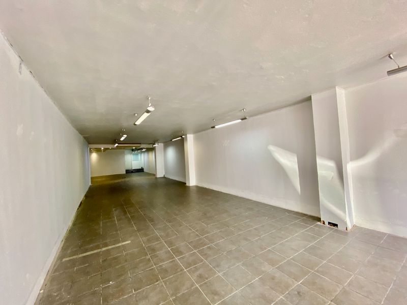 A vacant, open-plan commercial space featuring tiled flooring, structural columns, and overhead strip lighting, suitable for various retail or office configurations.