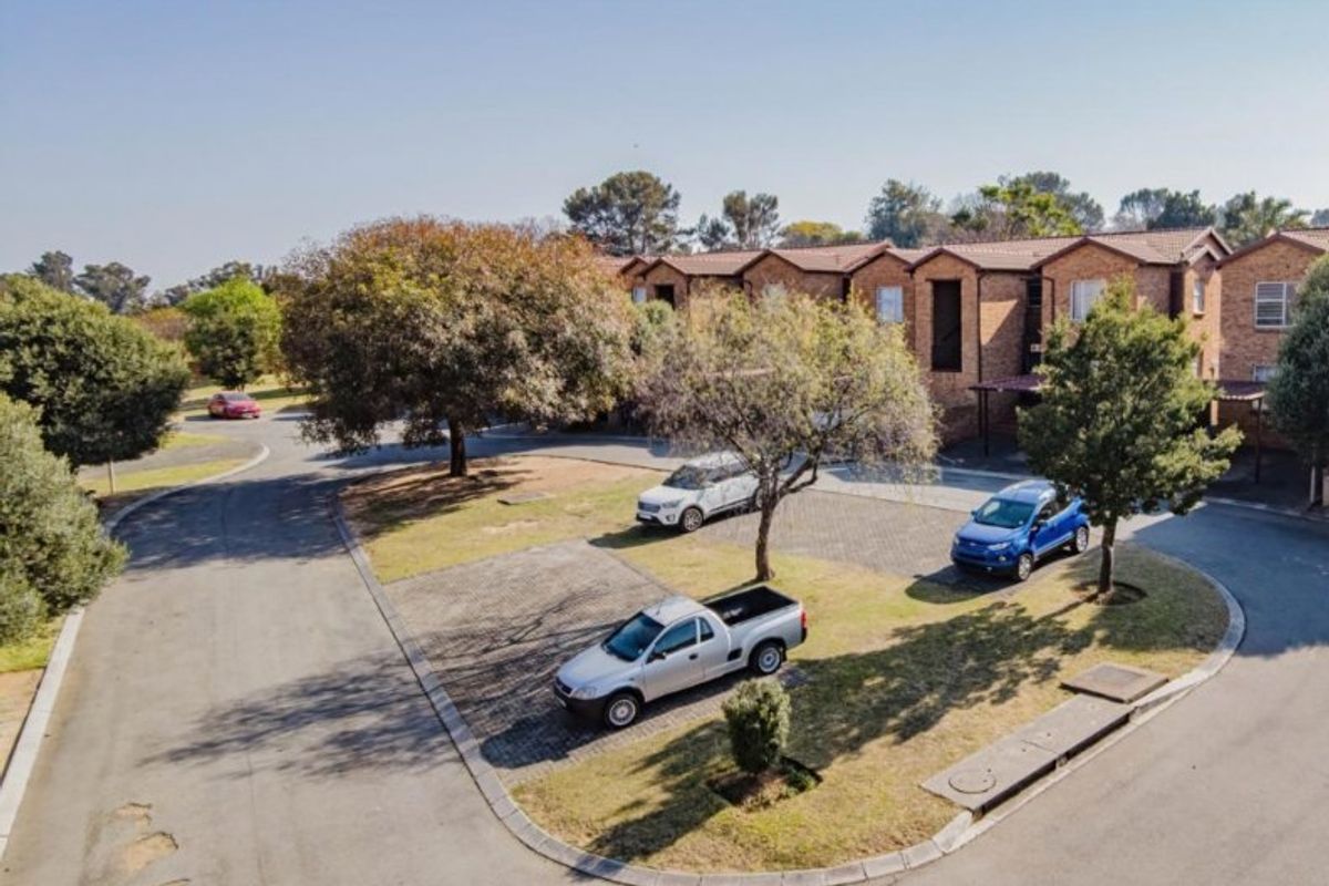 Aerial view of the apartment complex grounds, featuring paved parking areas, established trees, and brick building facades.