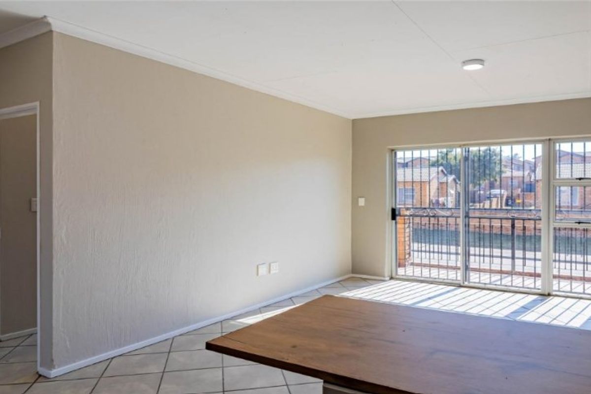 A bright, empty living area featuring tiled floors, a built-in cupboard, and a sliding glass door with security bars leading to an outdoor space.