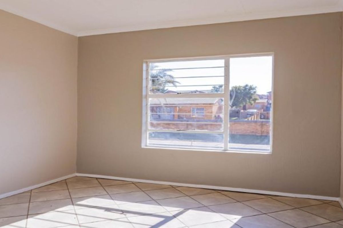 A bright, empty bedroom featuring neutral wall paint, tiled flooring, and a window fitted with security bars.
