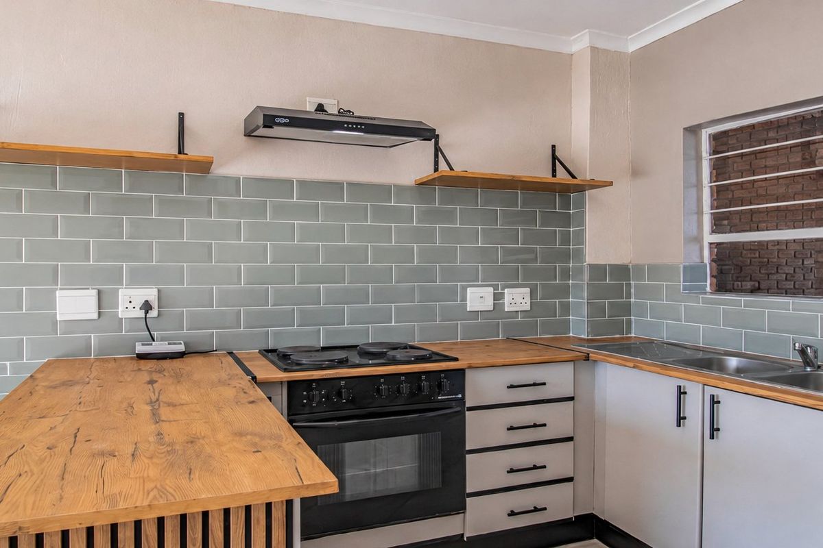 Modern kitchen featuring wooden countertops, subway tile backsplash, built-in oven with hob, extractor fan, and stainless steel sink, complemented by an exposed brick wall.