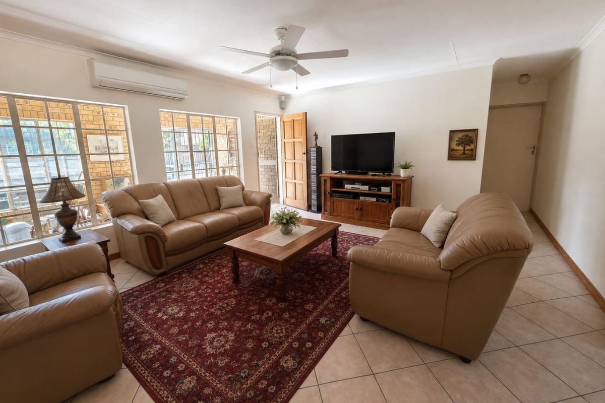 A comfortable living room featuring tiled flooring, a ceiling fan, and a split-system air conditioner, with natural light entering through large windows.