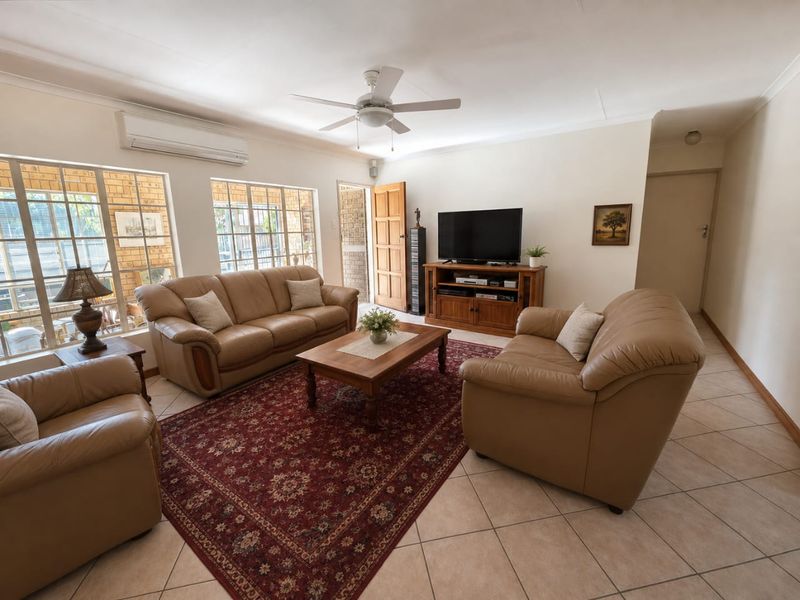 A comfortable living room featuring tiled flooring, a ceiling fan, and a split-system air conditioner, with natural light entering through large windows.