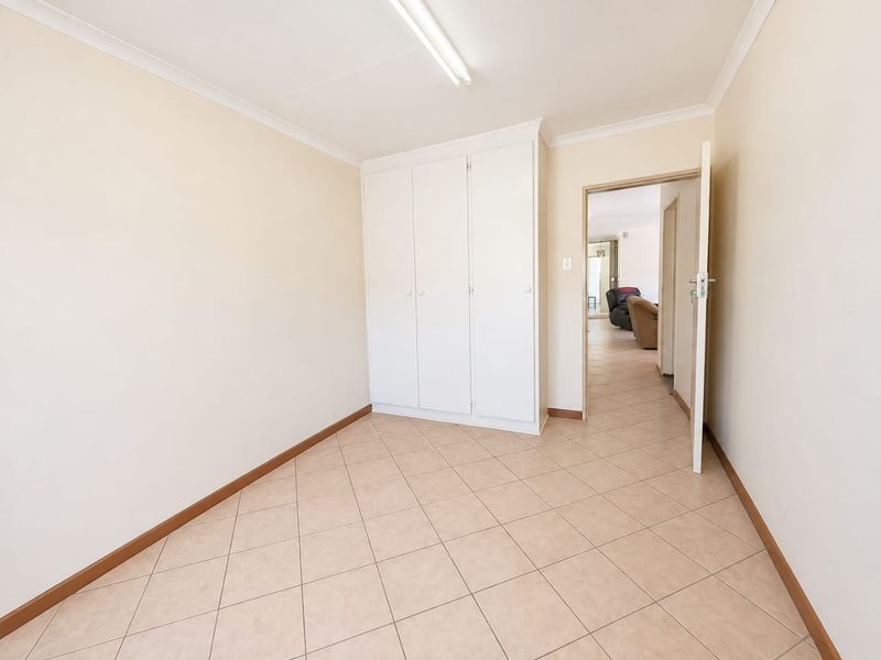 A clean, empty bedroom featuring neutral tiled flooring, built-in cupboards, and coved cornicing, offering a versatile space ready for personalization.