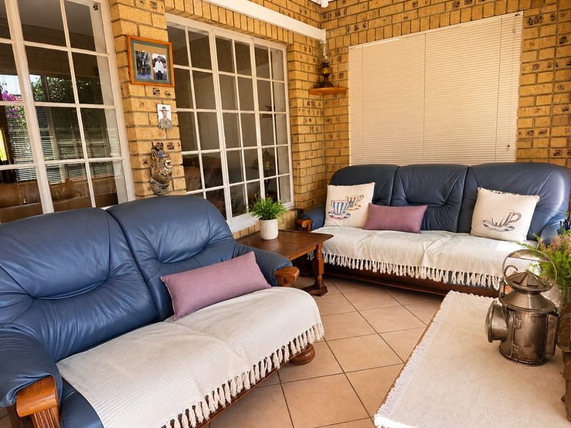 A covered patio area featuring exposed brick walls, tiled flooring, and large grid-pattern windows, providing a comfortable and enclosed outdoor living space.