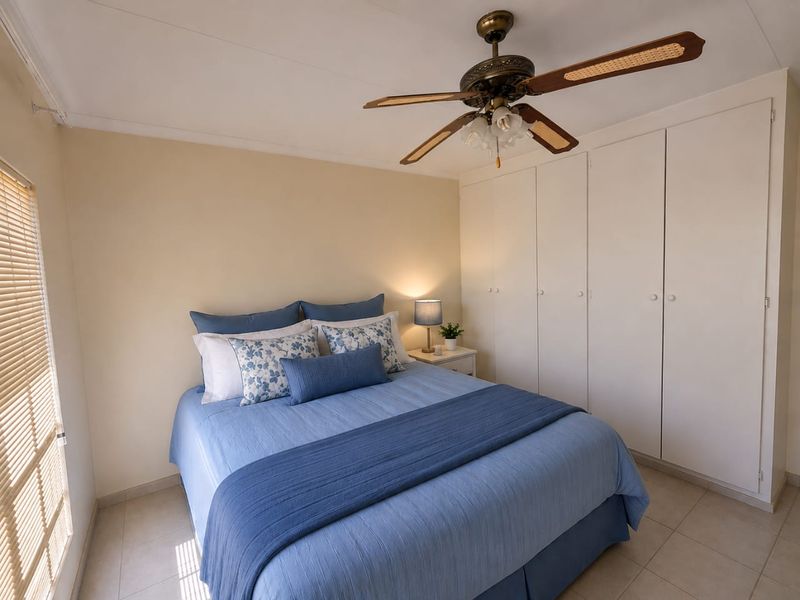A well-maintained bedroom featuring neutral tiled flooring, ample built-in cupboard storage, and a classic ceiling fan.