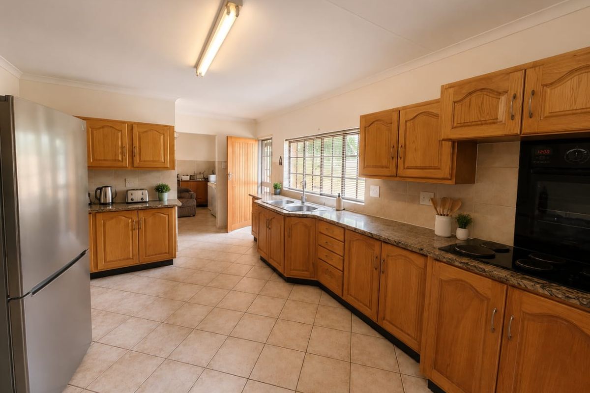 A functional kitchen featuring traditional wooden cabinetry, granite countertops, built-in oven, electric hob, and tiled flooring with direct access to a scullery area.