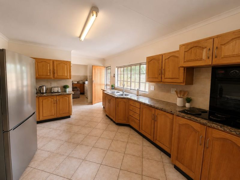 A functional kitchen featuring traditional wooden cabinetry, granite countertops, built-in oven, electric hob, and tiled flooring with direct access to a scullery area.
