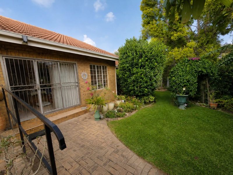 A well-maintained rear exterior featuring a brick facade, tiled roof, paved patio area, and a lush, established garden.