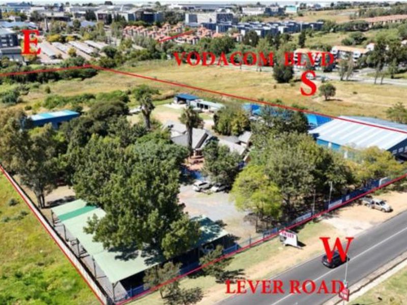 Aerial view of a commercial property site featuring multiple structures, mature landscaping, and perimeter fencing, situated near major road access.