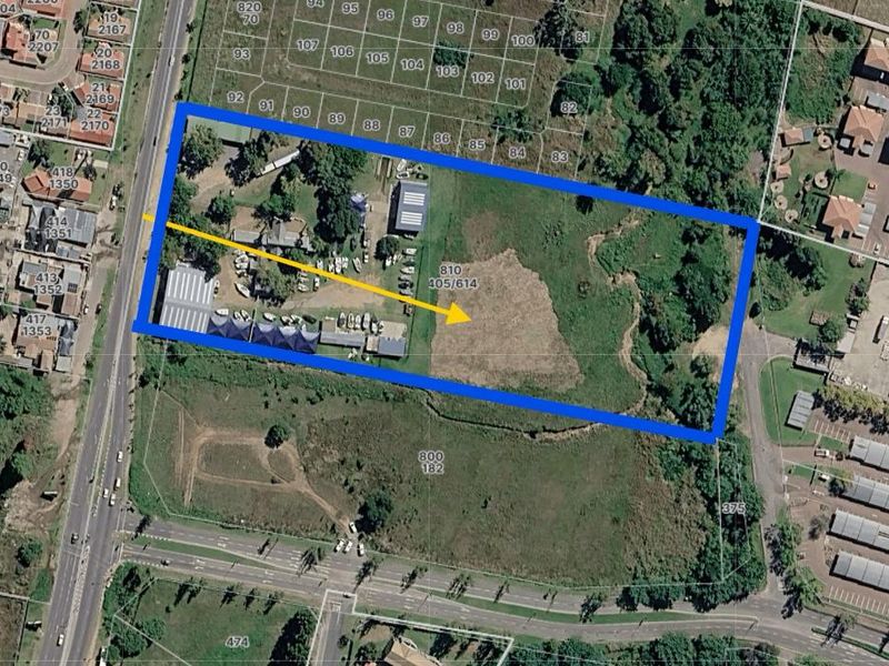 Aerial view of a commercial property plot with existing structures and significant undeveloped land, highlighting site boundaries and access.