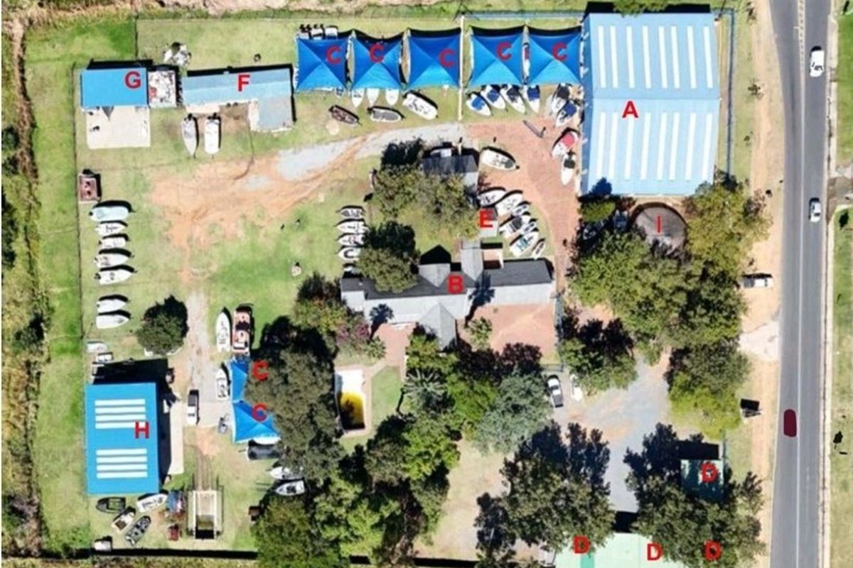 Aerial view of a commercial property featuring a large warehouse, multiple storage structures, shade ports, and a swimming pool on a spacious lot.