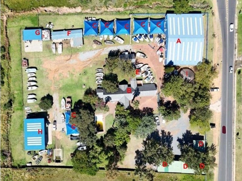 Aerial view of a commercial property featuring a large warehouse, multiple storage structures, shade ports, and a swimming pool on a spacious lot.