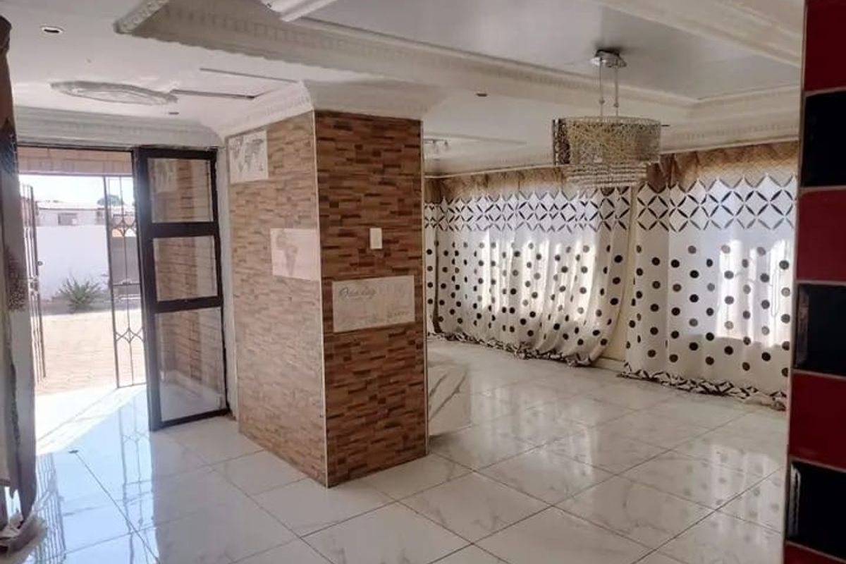 Spacious living area featuring polished marble-look floor tiles, a decorative stone-clad central pillar, and ornate ceiling cornices with recessed lighting.