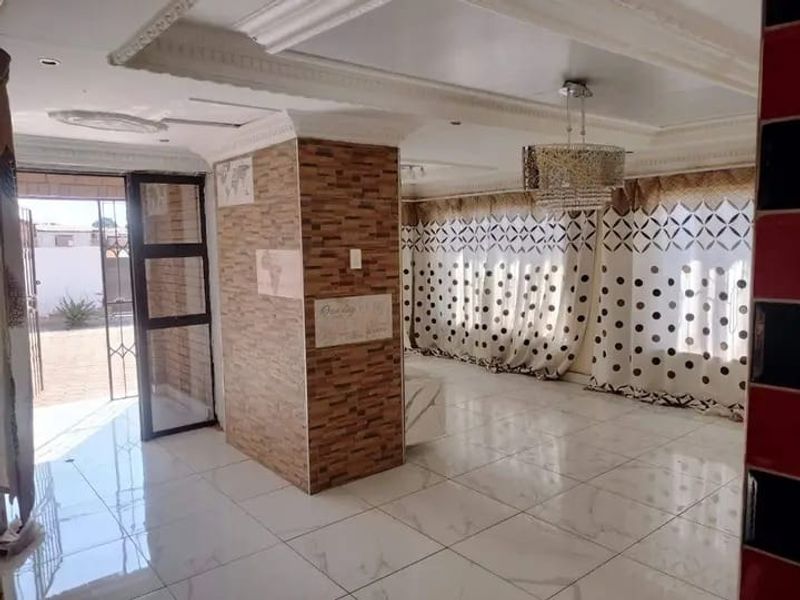 Spacious living area featuring polished marble-look floor tiles, a decorative stone-clad central pillar, and ornate ceiling cornices with recessed lighting.