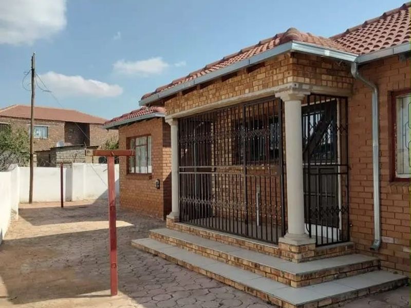 A rear exterior view of a face brick house featuring a covered patio area with security gates and a paved yard.
