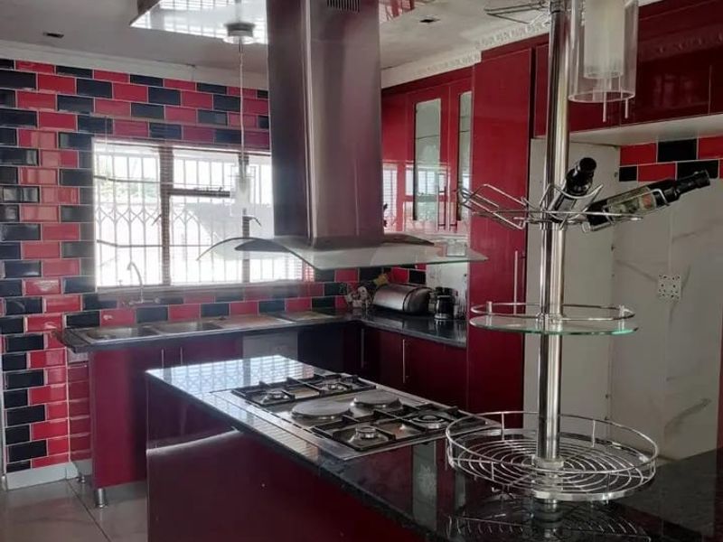 A kitchen featuring a central island with a gas cooktop, stainless steel extractor fan, granite countertops, and a distinctive red and black tiled backsplash.