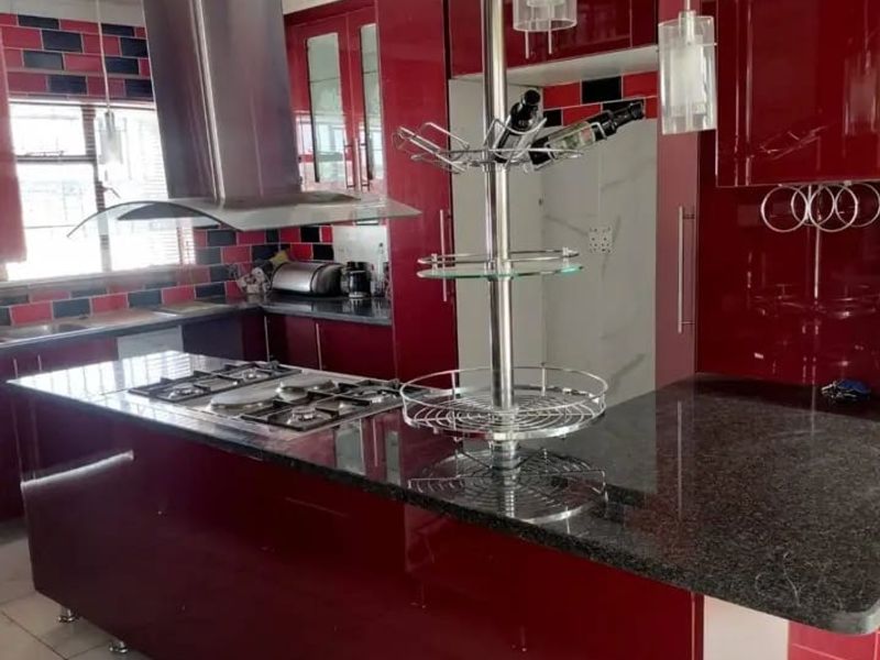Modern kitchen featuring high-gloss red cabinetry, a spacious granite island with a built-in gas hob, and a stainless steel extractor fan.