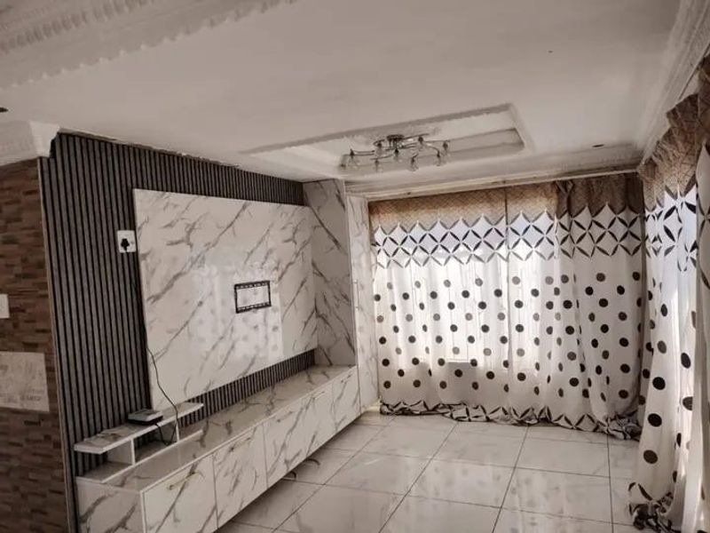 Living room featuring a custom built-in media unit with marble-effect finish, slatted wall detailing, recessed ceiling tray, and tiled flooring.