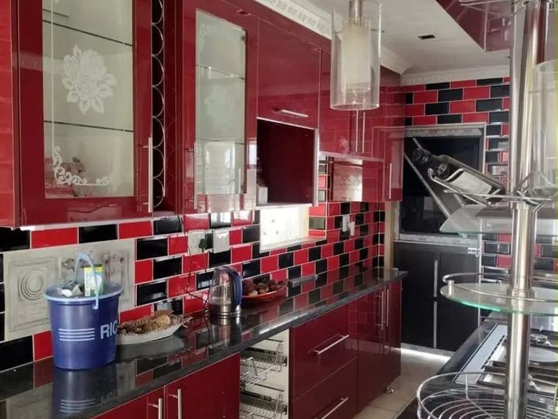 A modern kitchen featuring high-gloss red cabinetry, black granite countertops, and a distinctive black and red subway tile backsplash with integrated storage solutions.