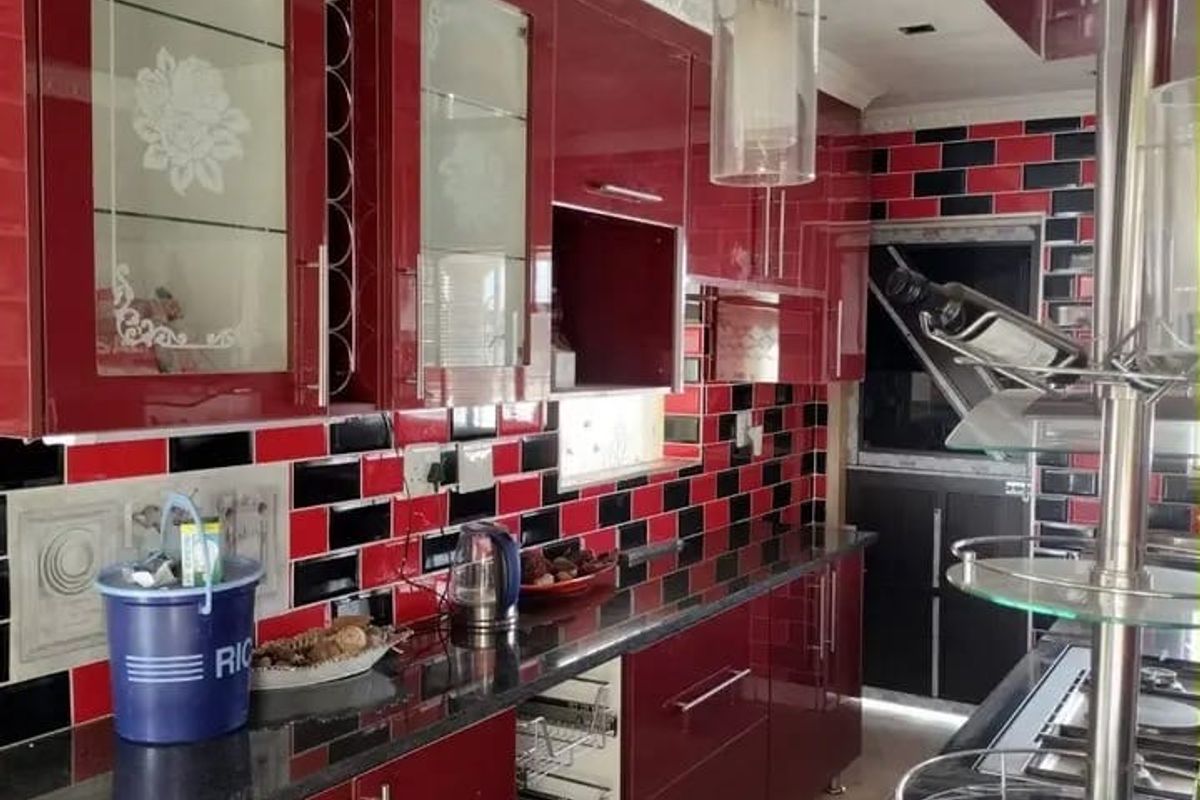 A modern kitchen featuring high-gloss red cabinetry, black granite countertops, and a distinctive black and red subway tile backsplash with integrated storage solutions.