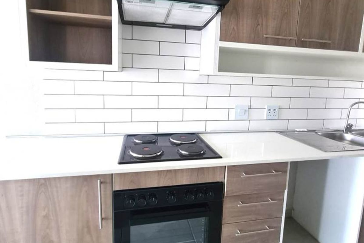 Modern kitchen featuring wood-finish cabinetry, white quartz countertops, subway tile backsplash, and integrated appliances including an oven, hob, and extractor fan.