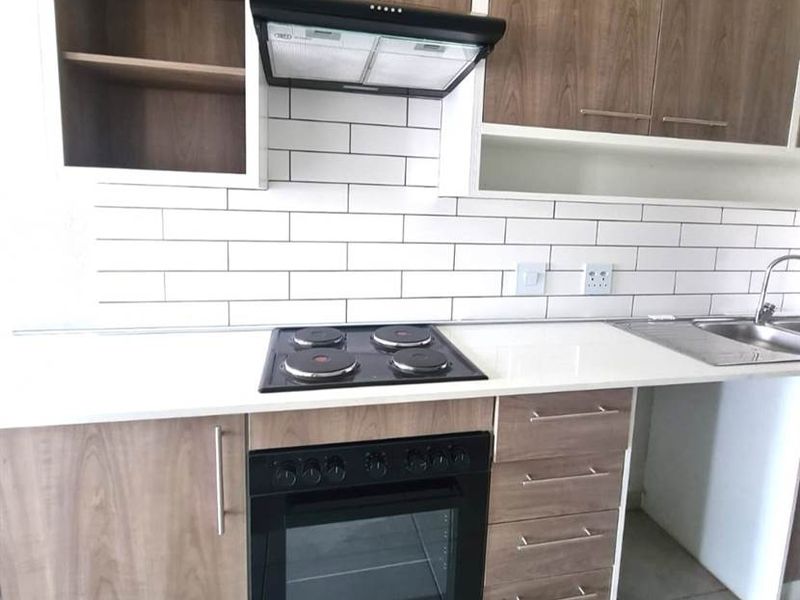 Modern kitchen featuring wood-finish cabinetry, white quartz countertops, subway tile backsplash, and integrated appliances including an oven, hob, and extractor fan.