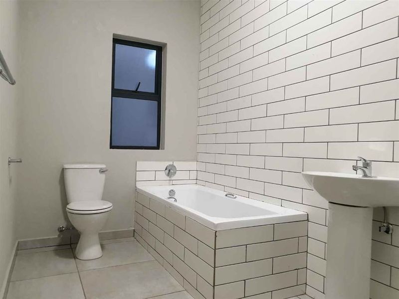 A clean, modern bathroom featuring a pedestal basin, a built-in bathtub with subway tile surround, and neutral floor tiling.