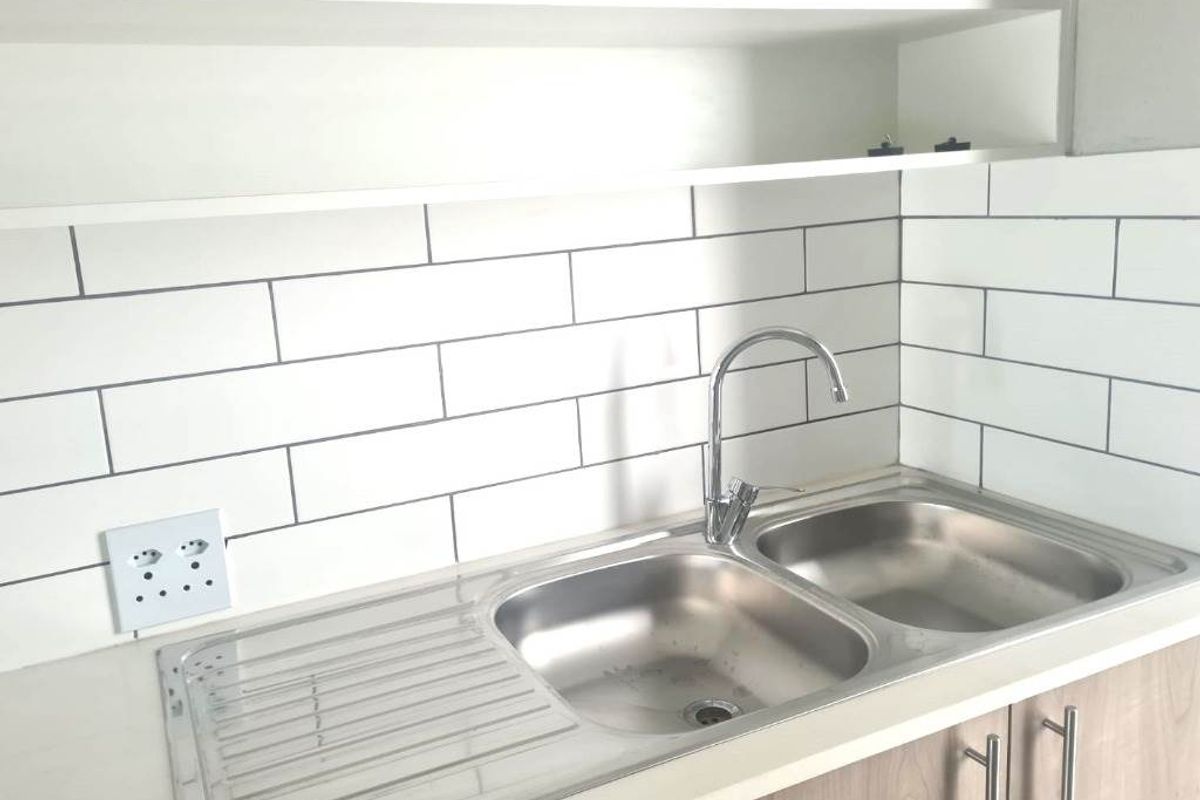 A clean, modern kitchen area featuring a stainless steel double sink, gooseneck faucet, and stylish white subway tile backsplash with wood-tone cabinetry.