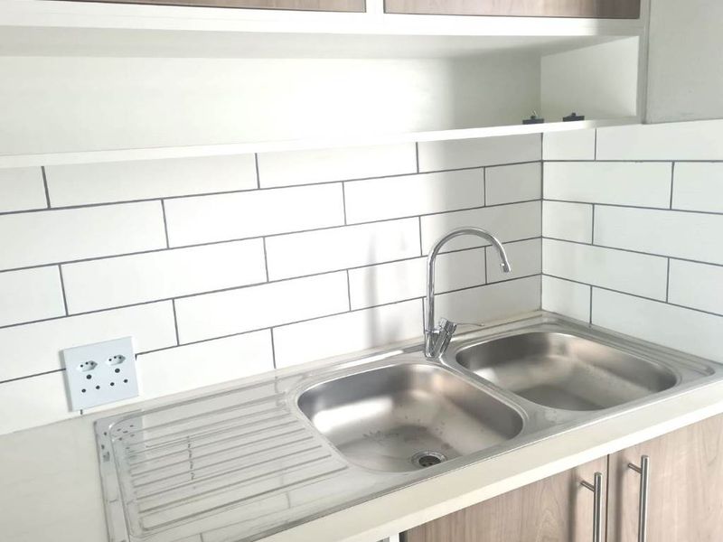 A clean, modern kitchen area featuring a stainless steel double sink, gooseneck faucet, and stylish white subway tile backsplash with wood-tone cabinetry.
