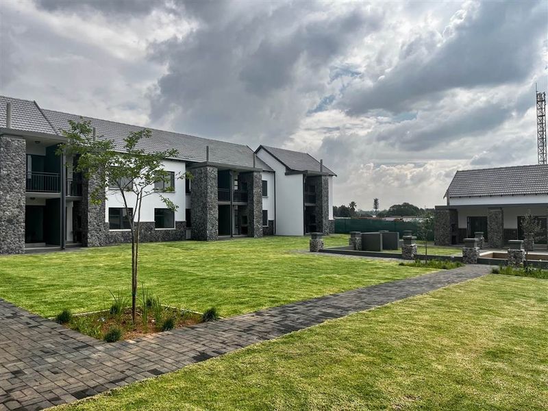 A well-maintained apartment complex exterior featuring stone-clad facades, tiled roofs, manicured lawns, and paved walkways with communal outdoor braai facilities.