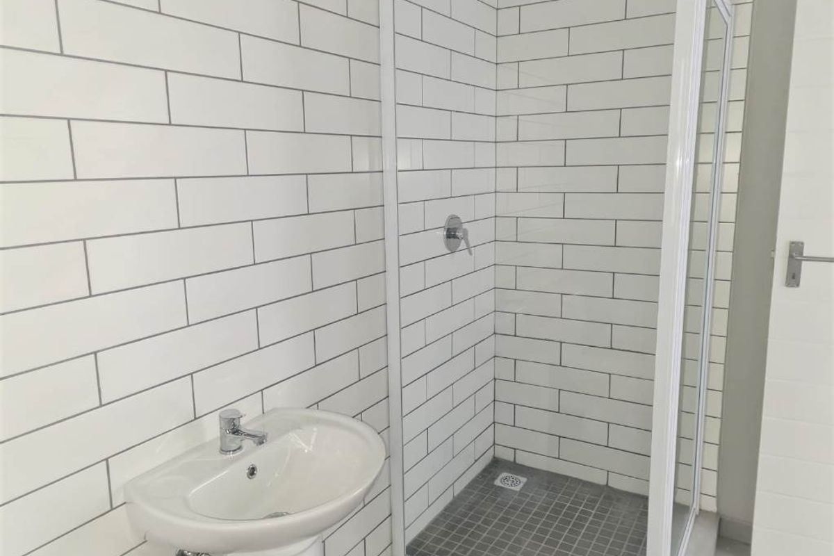 A clean, modern bathroom featuring a white pedestal basin, a glass-enclosed shower, and contemporary subway wall tiling.