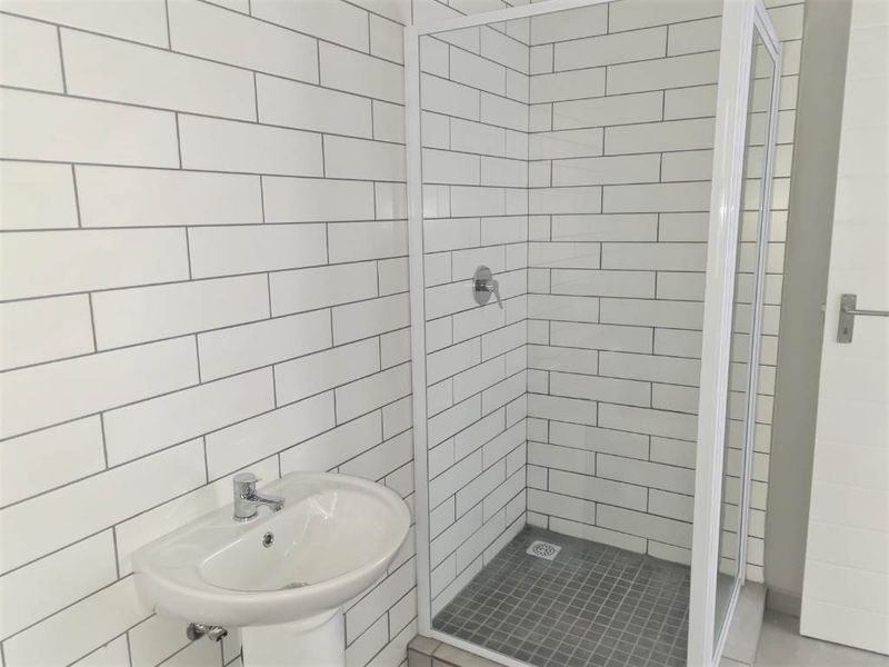 A clean, modern bathroom featuring a white pedestal basin, a glass-enclosed shower, and contemporary subway wall tiling.