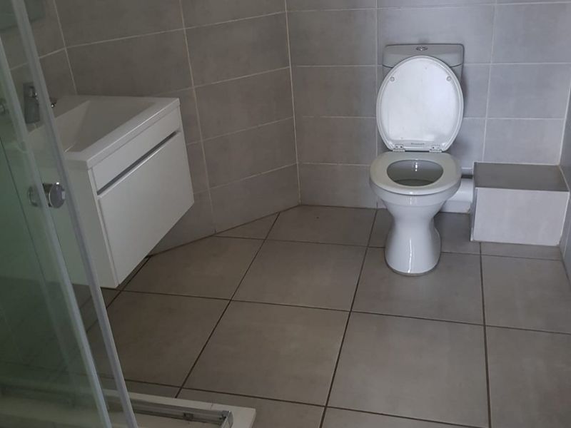 A clean, modern bathroom featuring a wall-mounted vanity, a glass-enclosed shower, and neutral floor-to-ceiling tiling.